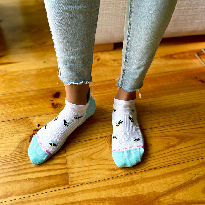 Ankle compression socks with a bee pattern, worn with light blue jeans on a wooden floor.