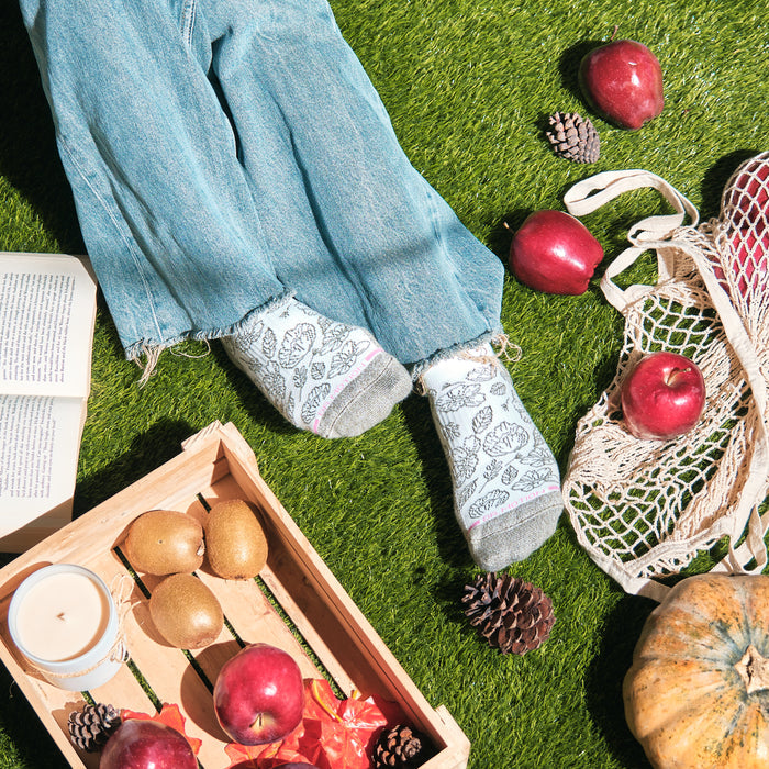 Ankle compression socks with a floral outline design, worn with frayed jeans on grass, surrounded by apples and a book.