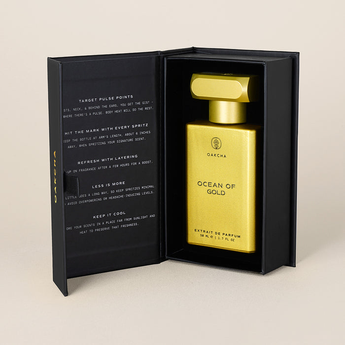 Three-quarter view of Ocean of Gold 50ml gold perfume bottle in open black presentation box on beige background