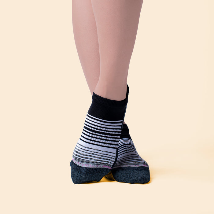 Ankle compression socks with an ombre stripe pattern in black, white, and gray, worn on a model's feet.