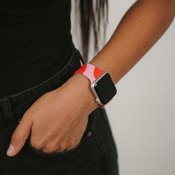 Pink and red abstract Coconut Lane Apple Watch strap worn on wrist, paired with black clothing, hand in pocket.