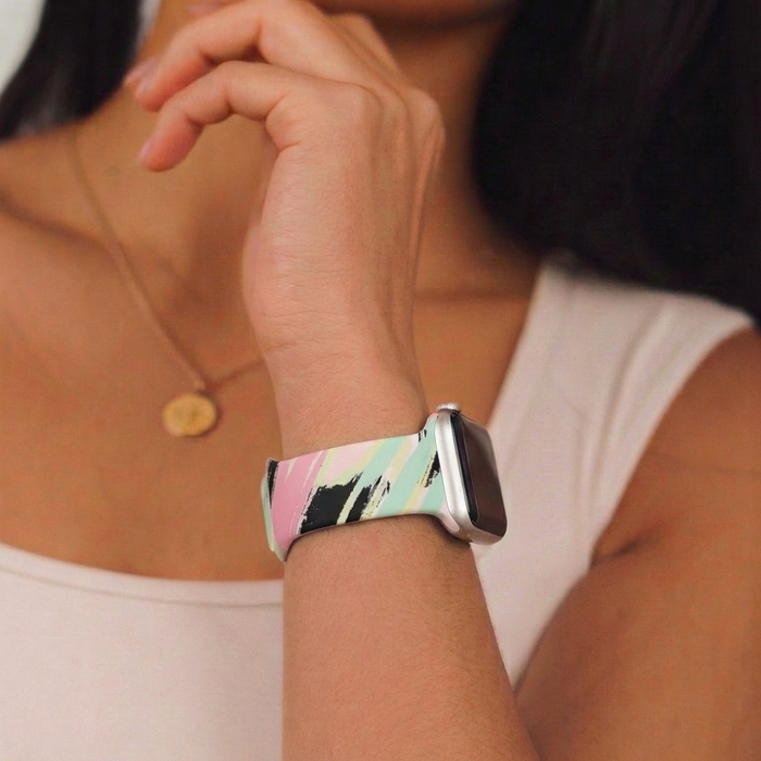 Coconut Lane Abstract Vibes Apple Watch strap with a colorful pattern, paired with a gold necklace featuring a round pendant.