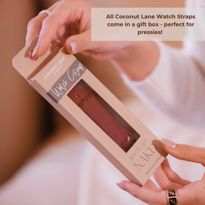 A pair of hands holds a boxed watch strap with the text "Abstract Vibes Apple Watch Strap" on the packaging. The strap, designed for Apple Watch models, is visible through a cut-out section. An overlay text reads, “All Coconut Lane watch straps come in a gift box - perfect for pressies!”