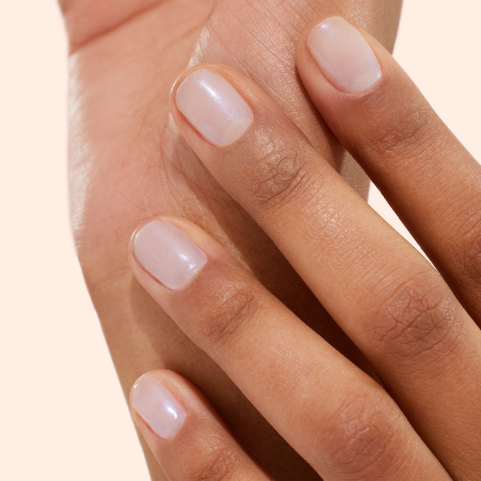 A close-up of a hand with neatly manicured nails painted with Manucurist’s Active™ Bright, a sheer, natural-colored bio-based polish, gently resting on another part of the hand against a light background, showcases the results of dedicated nail care.