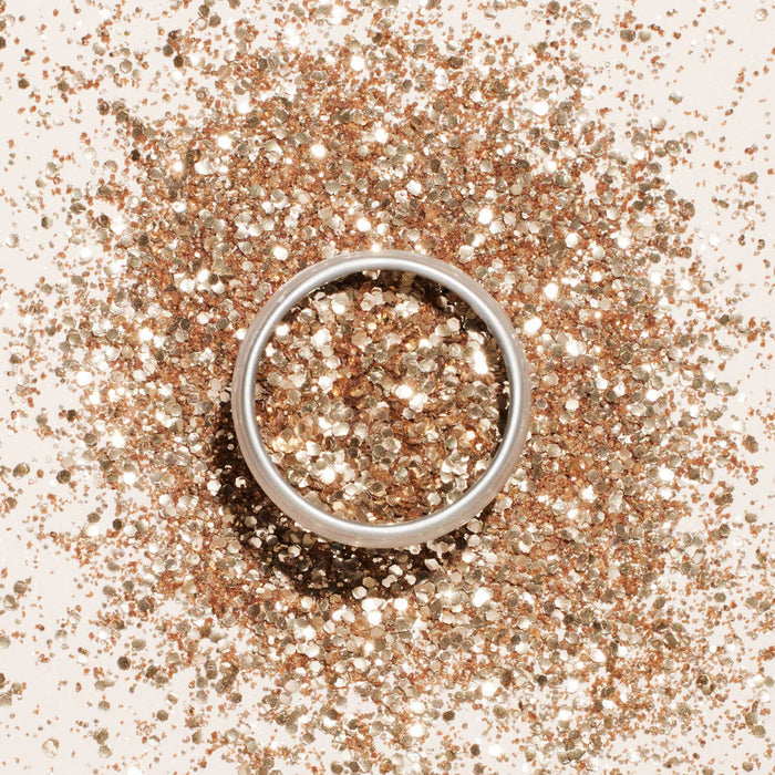 A silver ring rests on a surface sprinkled with Manucurist Biodegradable Glitter, creating a sparkling, festive, and eco-friendly background.