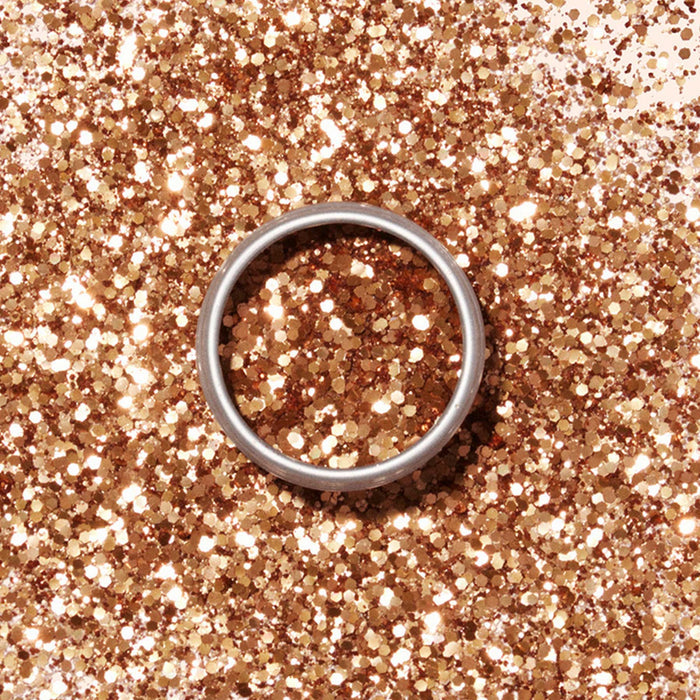 A silver ring rests on a surface dusted with Manucurist Biodegradable Glitter, creating a sparkling and festive gold backdrop.