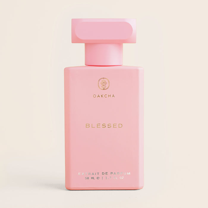 Front view of Blessed perfume bottle showing pale pink rectangular bottle with square cap and gold lettering on cream background
