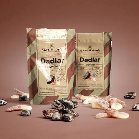 Dave & Jon's Dadlar Sour Cola bags with sour cola flavored dates scattered on a dark pink background