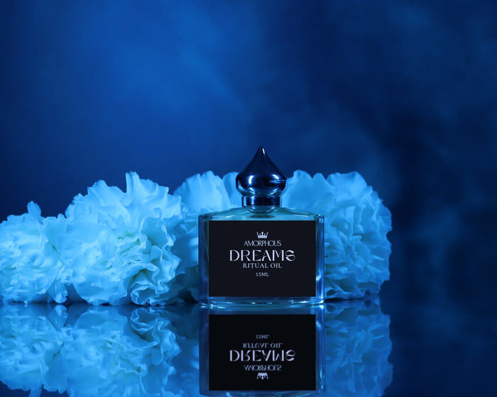 Perfume bottle labeled 'Dreams' on a reflective surface with blue flowers in the background