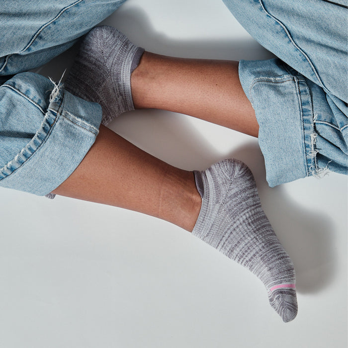 Ankle compression socks in gray worn with rolled-up denim jeans, showing feet positioned together on a white background.