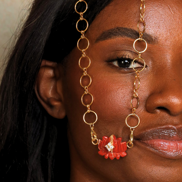 A model showcasing the Jasper Lotus Charm, a terracotta-red jasper flower with gold accents and crystals, elegantly worn as a necklace.