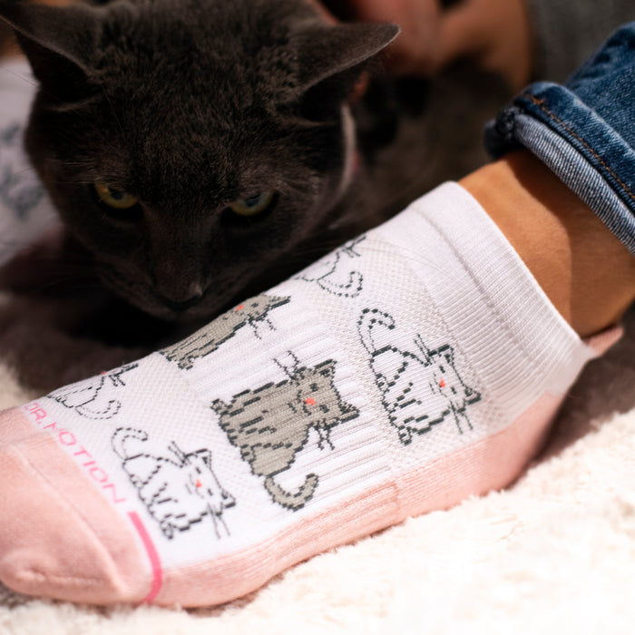 Ankle compression sock with a cat design, worn on a foot next to a gray cat on a soft surface.
