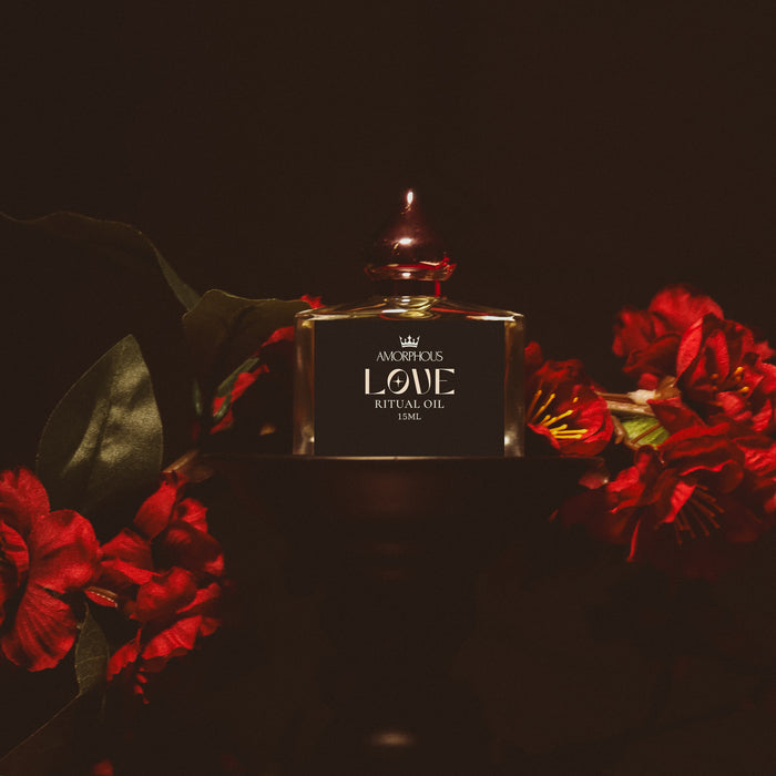 Perfume bottle labeled 'Amorphous Love Ritual Oil' surrounded by red flowers on a dark background