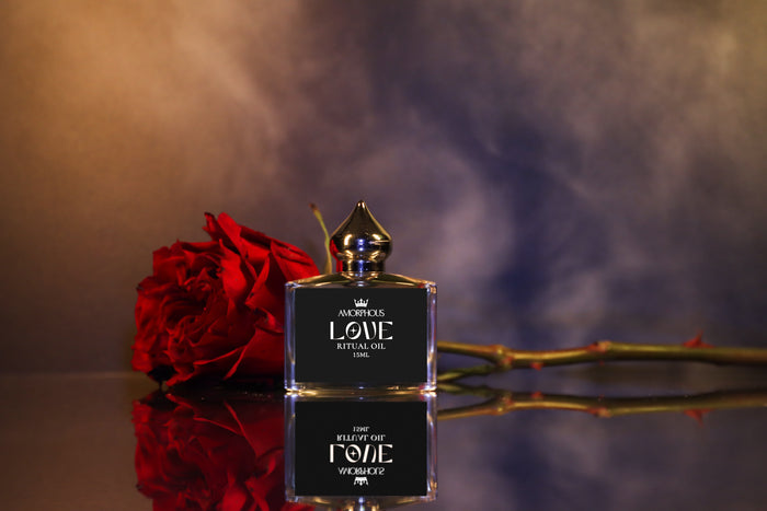 Perfume bottle labeled 'Love Ritual Oil' with a red rose on a reflective surface
