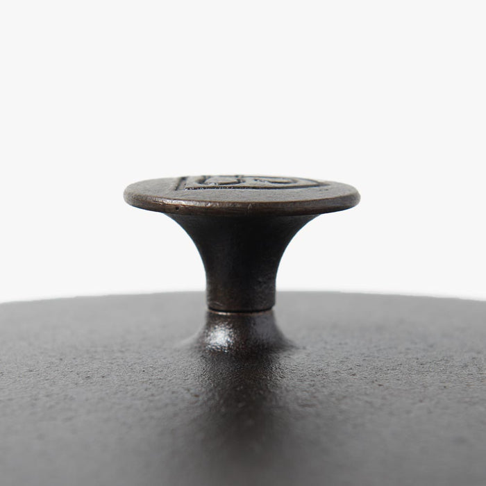 Close-up side view of the cast iron knob on the Field Skillet Lid, flared top over a pebbled lid surface