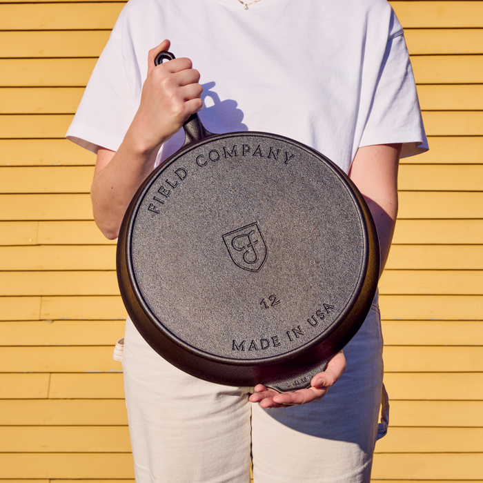 Person holding the No.12 Field Cast Iron Skillet upside down to show its stamped underside, outdoors in sunlight