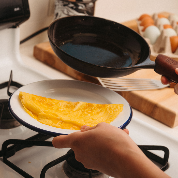 Person slides a folded omelette from the No.5 Field Chef Skillet onto a plate at the stovetop
