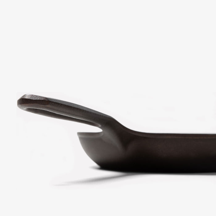 Close-up profile of the Field Skillet handle and hanging hole, curved wall rising behind