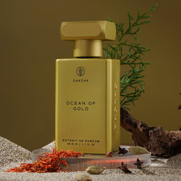 Front of Ocean of Gold perfume bottle; gold rectangular bottle with cap and OAKCHA logo on sandy surface with spices