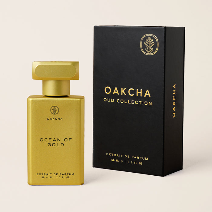 Angled view of Ocean of Gold perfume showing gold rectangular bottle and cap beside black Oakcha box on cream background