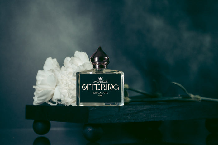 Perfume bottle labeled 'Offering' with white flowers on a dark background
