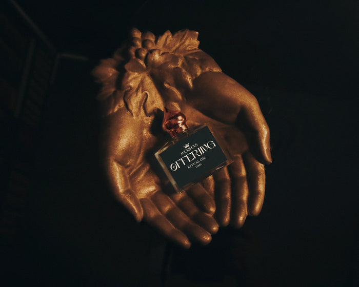 A bottle of ritual oil labelled "offering" sitting in a hand shaped copper dish.