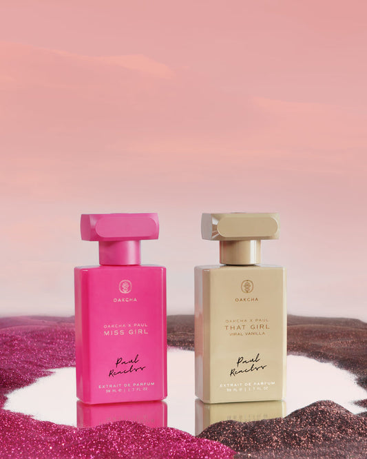 Front view of Paul Reactss - The Girls perfume bottles showing pink and beige glass bottles with gold caps on a pink glitter backdrop