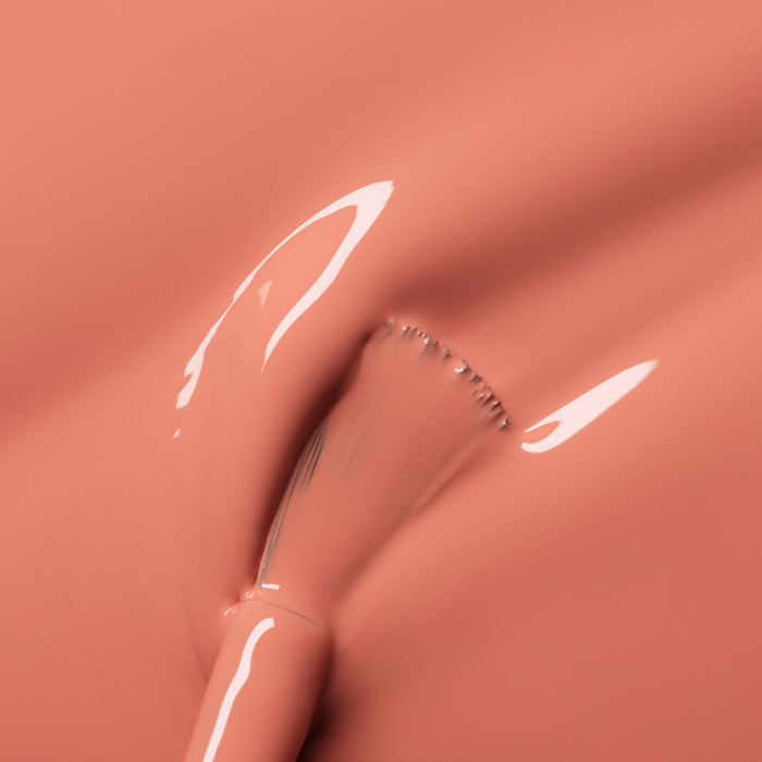 A close-up shows a brush spreading Manucurist Peach nail polish, creating smooth, shiny streaks of peachy orange tint across the liquid surface.