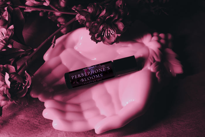 Persephone's Blooms perfume bottle on a pink ceramic dish with flowers in the background