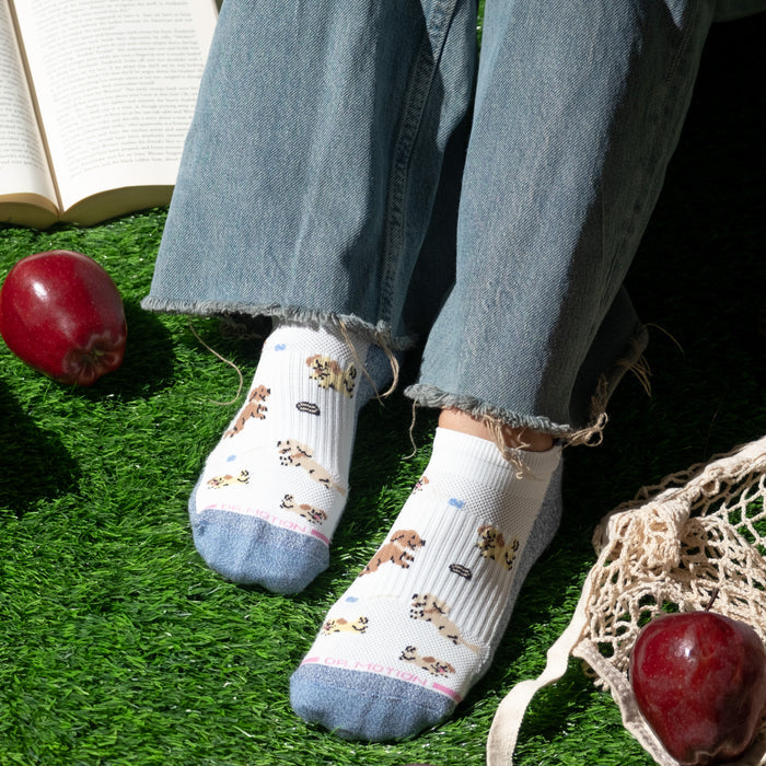 Ankle compression socks featuring playful dog designs, worn with frayed denim jeans on grass.