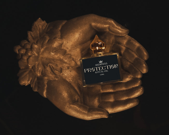 Perfume bottle labeled 'PROTECTION' held by a bronze hand against a black background