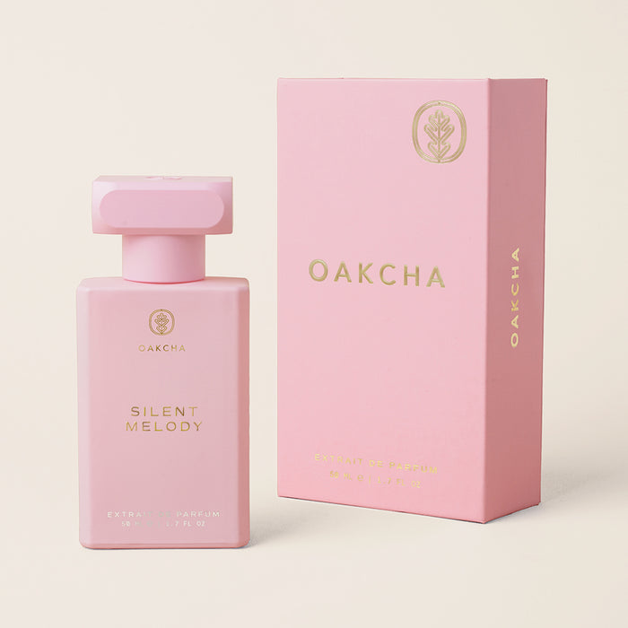 Front view of Silent Melody perfume bottle and matching pink box showing gold embossed logo and gold cap on beige background