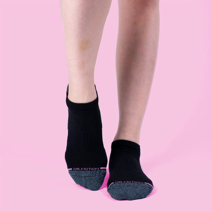Black ankle compression socks with a half-cushion design and gray toe, displayed against a pink background.