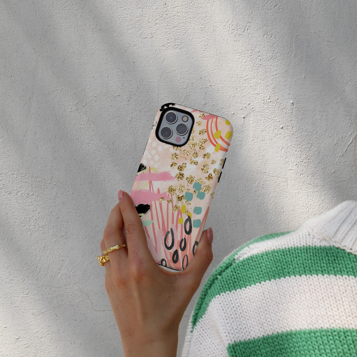 Hand holding Coconut Lane Tough Phone Case with abstract pattern; person in green-striped sweater stands by a light wall.