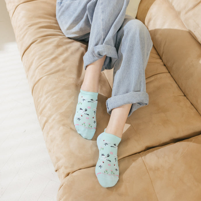 Ankle compression socks with a light blue background and a whooping crane and floral design, worn with rolled-up jeans.