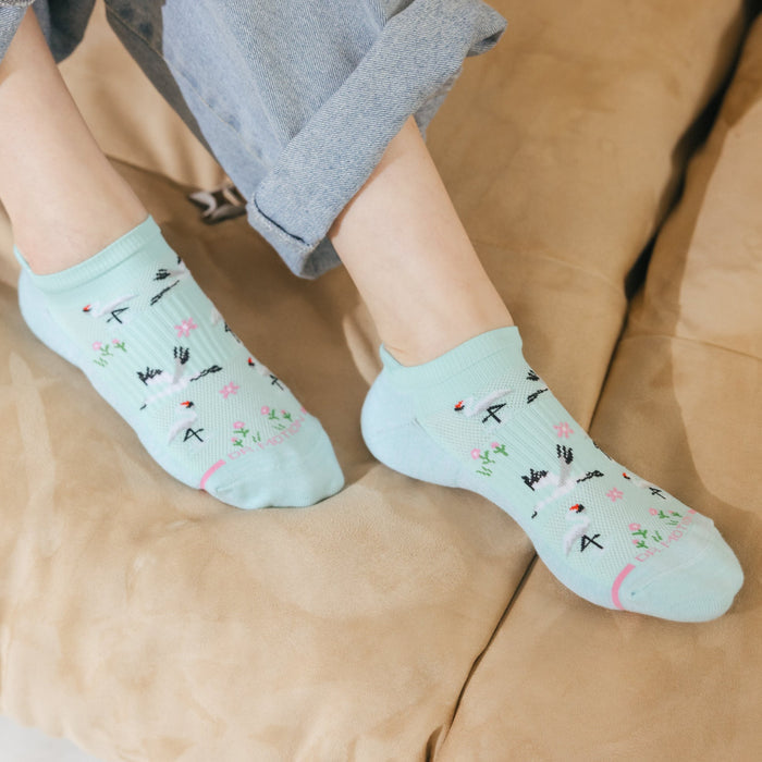 Light blue ankle compression socks with a whooping crane and floral pattern, worn on a person's feet.